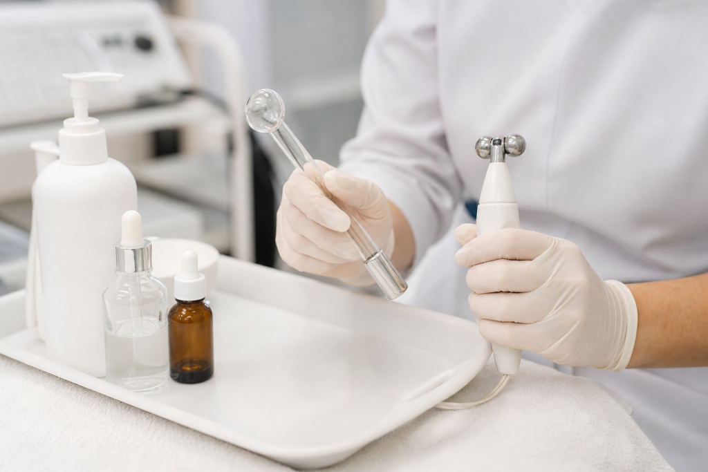 Gloved hands holding a high-frequency electrode with galvanic tool and serums on tray.