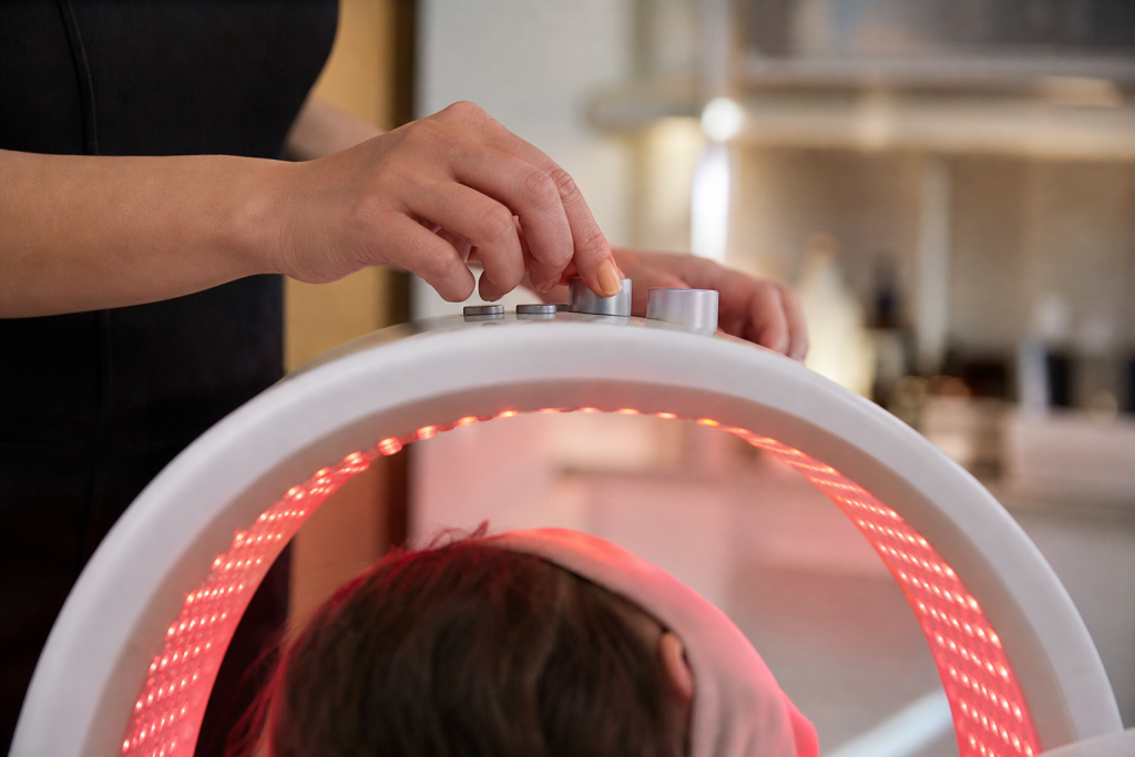 Hands adjusting controls on an LED light therapy panel with red/near-infrared glow.