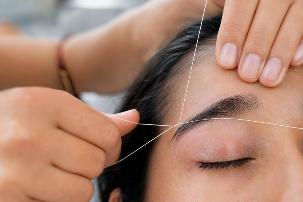 Technician performing eyebrow threading with a twisted cotton thread near a client's eyebrow.